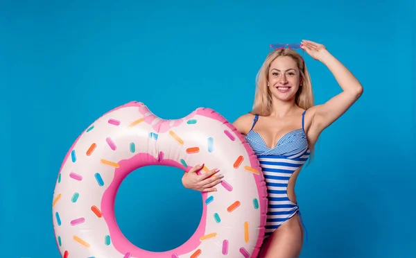 Foto de mujer feliz en traje de baño a rayas con donut salvavidas sobre fondo azul vacío — Foto de Stock