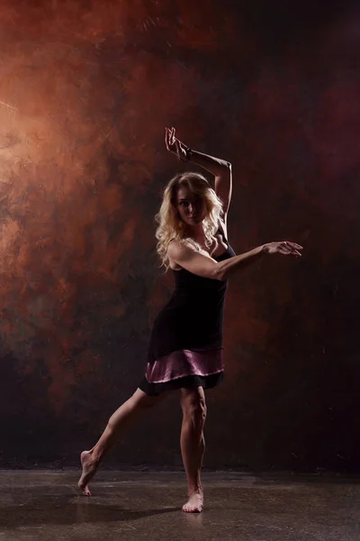 Foto de larga duración de la joven rubia bailando en vestido negro sobre fondo marrón — Foto de Stock