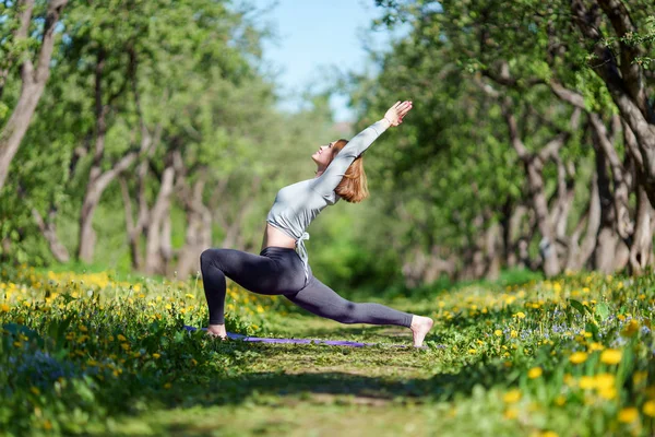 Foto en el costado de una joven con los brazos levantados practicando yoga en el bosque —  Fotos de Stock