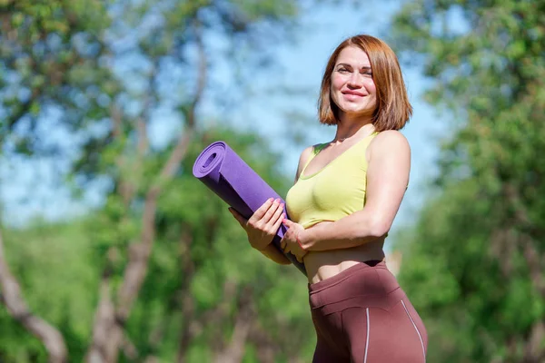 Portret van Happy yoga vrouw met paarse mat in handen in bos — Stockfoto