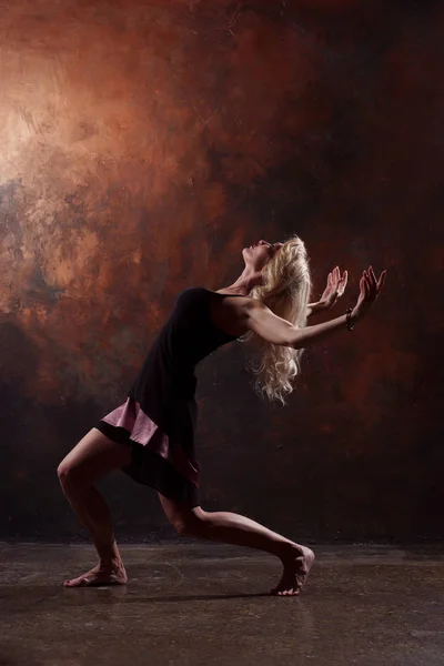 Foto de dança loira olhando para trás em vestido preto no fundo marrom — Fotografia de Stock