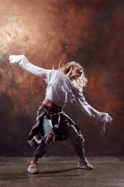 Koyu kahverengi arka plan üzerinde yırtık kot pantolon ve spor ayakkabı gelişen saç ile ince sarışın dansçı Görüntü