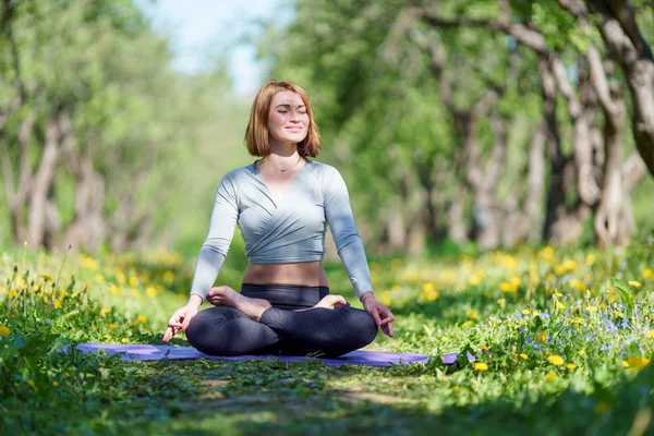 Photo of girl doing yoga sitting in lotus position on blue rug in woods — Stock Photo, Image