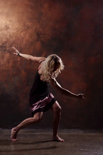 Foto de larga duración de la joven bailarina en vestido negro corto sobre fondo marrón —  Fotos de Stock