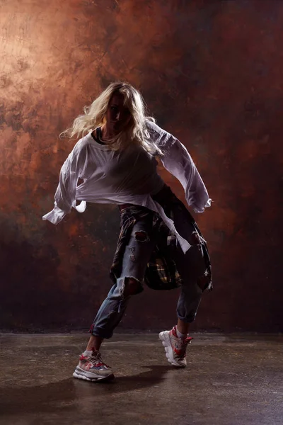 Φωτογραφία του νεαρό χορό ξανθιά γυναίκα σε άρπαξαν τζιν και αθλητικά παπούτσια σε καφέ φόντο — Φωτογραφία Αρχείου
