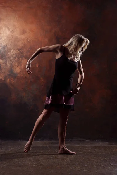 Foto de cuerpo entero de rubia bailando en vestido negro corto sobre fondo marrón — Foto de Stock