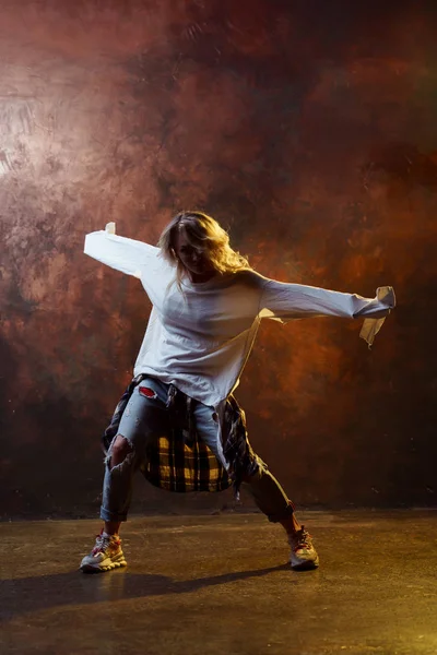 Foto de dança de cabelos longos menina loira em jeans azul rasgado no fundo marrom — Fotografia de Stock