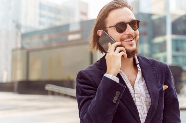 Şehirde yürürken telefonla konuşurken güneş gözlüğü takan adamın fotoğrafı