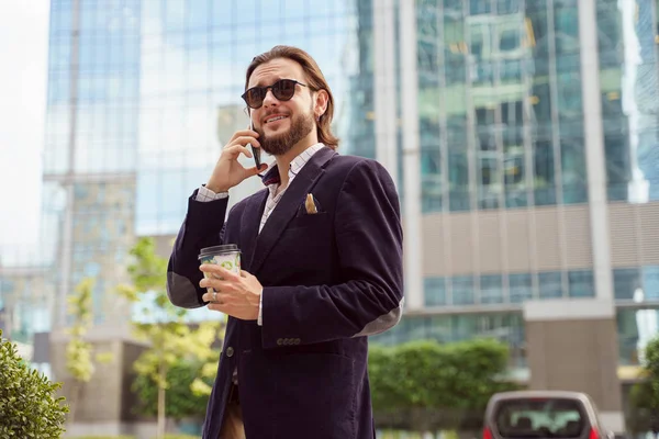 Foto di felice uomo bruno in occhiali da sole che parla al telefono mentre cammina in città — Foto Stock