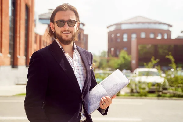 Foto di uomo allegro in occhiali da sole e giacca con computer portatile in piedi in città in primavera — Foto Stock