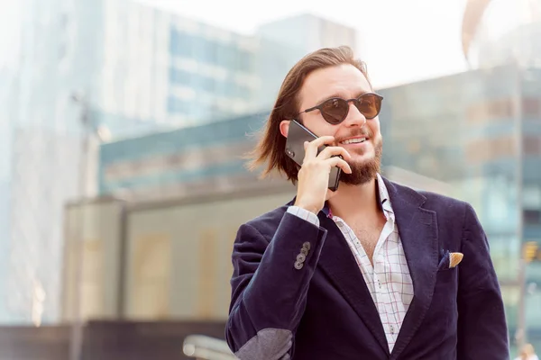 Foto eines brünetten Mannes mit Sonnenbrille, der beim Spazierengehen in der Stadt telefoniert — Stockfoto
