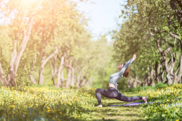 Foto de una mujer con los brazos levantados practicando yoga en el bosque durante el día —  Fotos de Stock