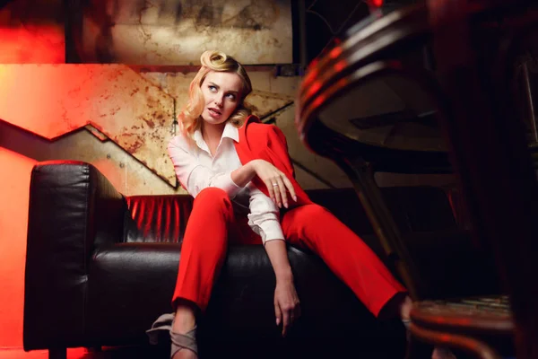 Full-lenght portrait of blonde woman in red jacket sitting on leather sofa — Stock Photo, Image