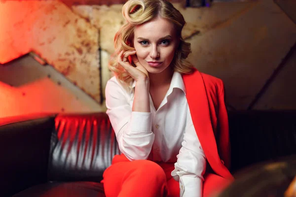 Foto van Happy blonde in rode jas zittend op lederen sofa — Stockfoto