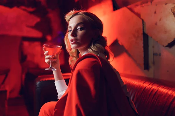 Foto av ung blondin i röd jacka med cocktail i hennes hand i nattklubb — Stockfoto