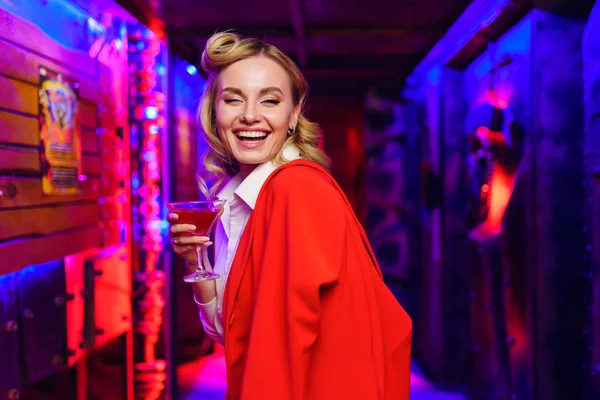 Фото блондинки с коктейлем в руке на красно-синем фоне — стоковое фото
