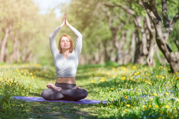 Ormanda mavi halı üzerinde lotus pozisyonda oturan kolları ile yoga yapan kadın görüntü — Stok fotoğraf