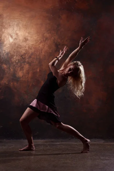 Foto de larga duración de una bailarina joven que mira hacia arriba en vestido negro corto sobre fondo marrón — Foto de Stock