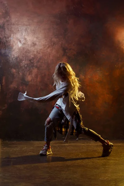 Foto de dança menina loira em jeans azul rasgado no fundo marrom — Fotografia de Stock