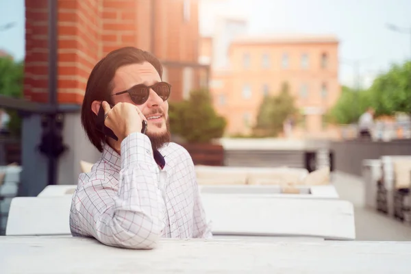 Foto del hombre hablando por teléfono sentado en la cafetería de la calle en la ciudad en la tarde de verano — Foto de Stock