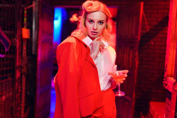 Фото серьезной блондинки с коктейлем в руке на красном и синем фоне — стоковое фото