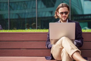 Yaz günü şehir merkezinde ahşap bankta oturan dizüstü bilgisayar ile adam freelancer Fotoğrafı
