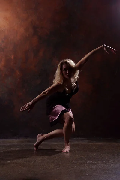 Foto de mujer rubia bailando joven en vestido negro sobre fondo marrón — Foto de Stock