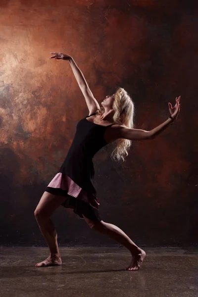 Foto de rubia bailando mirando atrás en vestido negro sobre fondo marrón en el estudio — Foto de Stock