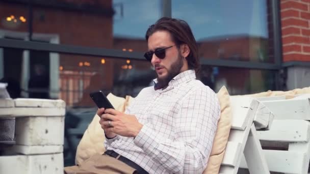 Vousatý muž na slunečních brýlích a typy na smartphone — Stock video