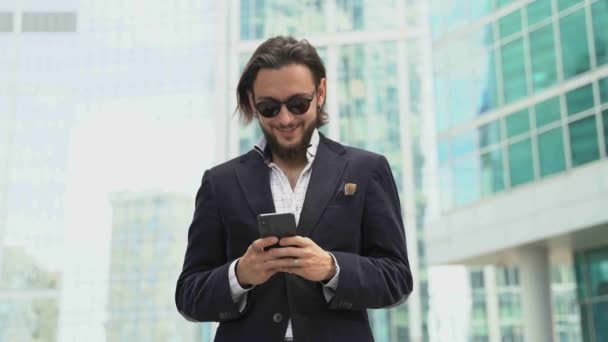 Homem de negócios em tipos de terno preto no smartphone e sorrisos — Vídeo de Stock