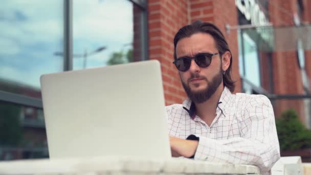 Hombre de negocios serio en tipos de gafas de sol en el ordenador portátil y cheques — Vídeo de stock
