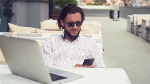 Guy types on black smartphone sitting at white table — Stock Video