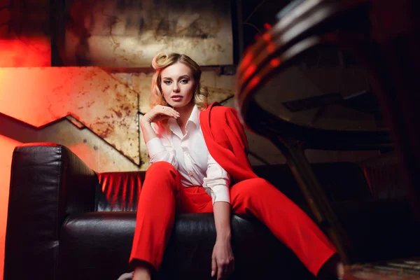 Retrato completo de jovem loira de jaqueta vermelha sentada no sofá de couro — Fotografia de Stock