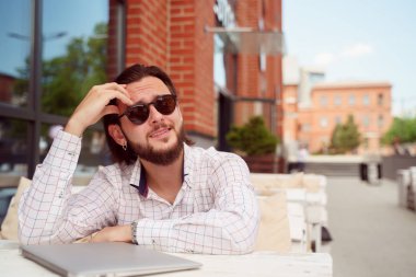 Şehirde açık kafede dizüstü bilgisayar ile masada oturan güneş gözlüğü brunet adam Fotoğrafı