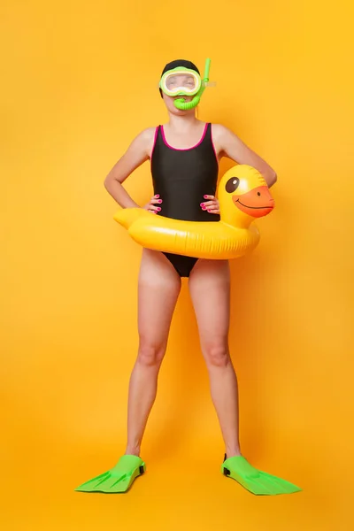 Foto de chica nadadora en traje de baño negro en aletas con boya salvavidas infantil en forma de patito sobre fondo naranja — Foto de Stock