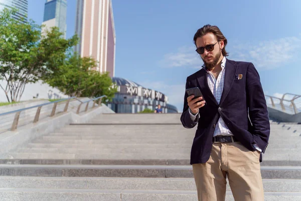 Foto eines Mannes mit Sonnenbrille und Handy in der Hand bei einem Spaziergang in der Stadt — Stockfoto