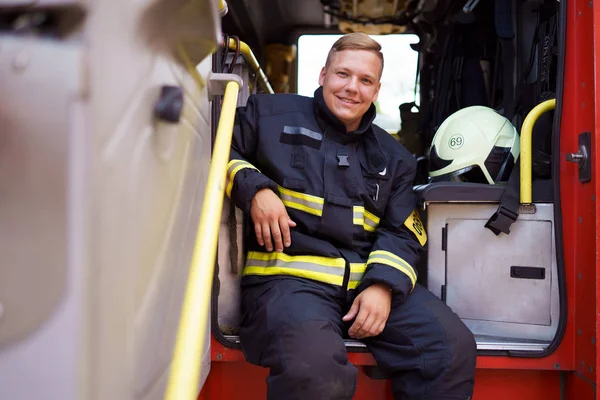 Imagen de bombero sonriente sentado en camión de bomberos en la estación de bomberos —  Fotos de Stock