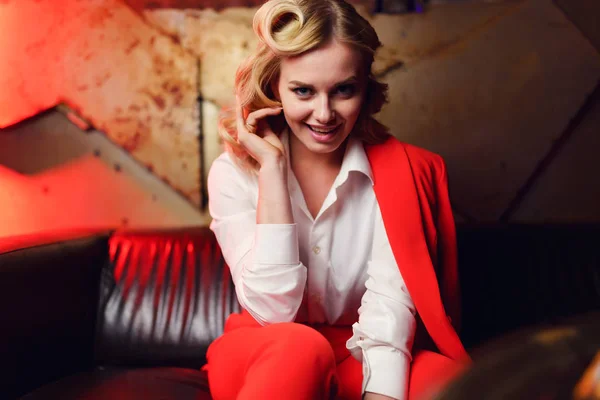 Photo of young blonde in red jacket sitting on leather sofa — Stock Photo, Image