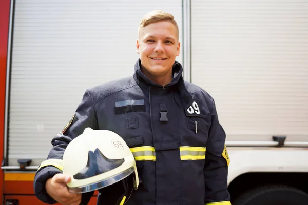 Foto av lycklig brandman med hjälm i handen stående nära brandbil — Stockfoto