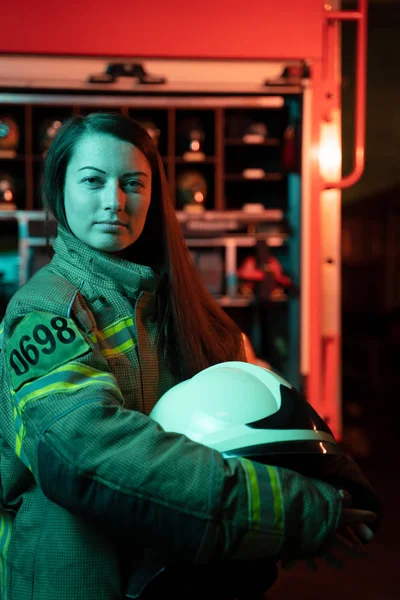 Foto von Feuerwehrmädchen mit langen Haaren und Helm in der Hand am Feuerwehrhaus. — Stockfoto