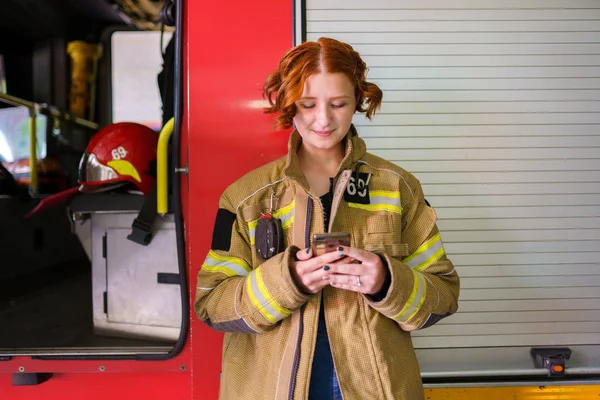 Imagen de mujer bombero con teléfono en las manos contra el fondo del camión de bomberos — Foto de Stock