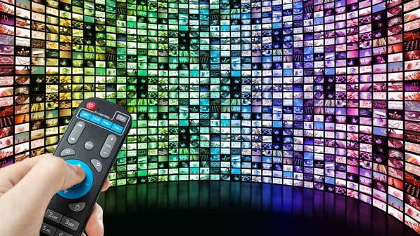 Obrázek velké obrazovky s mnoha vícebarevnými kanály, ruce muže s dálkovým ovládáním. — Stock fotografie