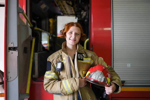 Foto de mujer bombero con casco en las manos contra el telón de fondo de camión de bomberos —  Fotos de Stock