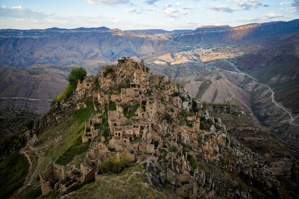 Фото древних руин горной местности с зеленой растительностью на фоне облачного голубого неба
