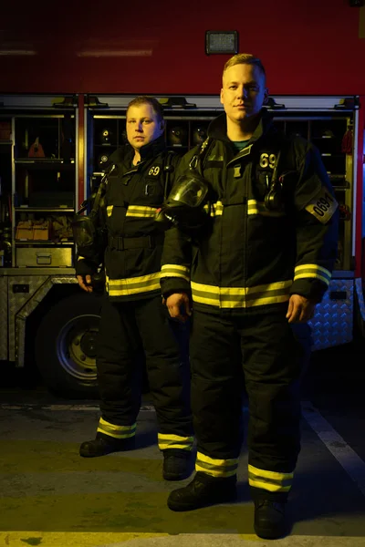 Imagen completa de dos bomberos mirando a la cámara cerca de camión de bomberos , — Foto de Stock