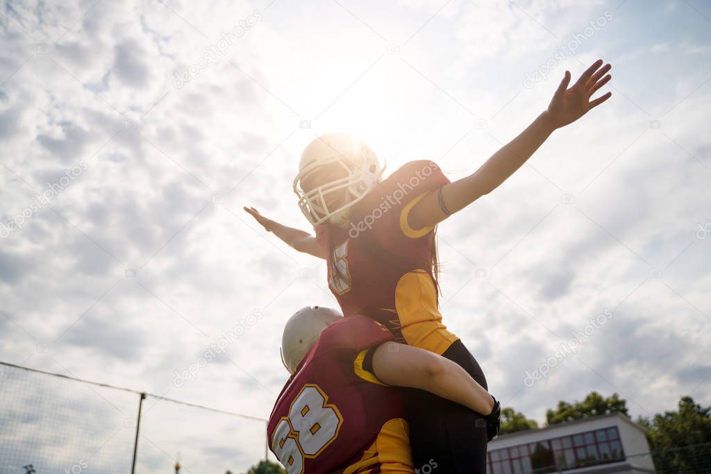 Photo of two American football woman athletes wearing helmets with their hands to side against cloudy sky