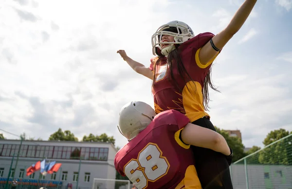 Bild zweier amerikanischer Fußballerinnen, die Helme mit den Händen zur Seite gegen den bewölkten Himmel tragen — Stockfoto