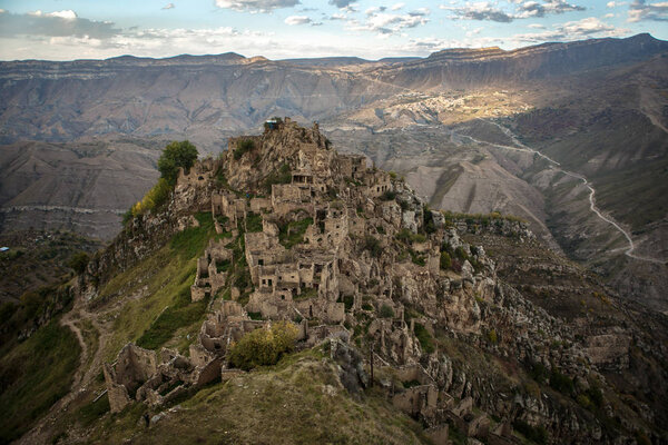 Изображение древних руин горной местности с зеленой растительностью на фоне облачного голубого неба
