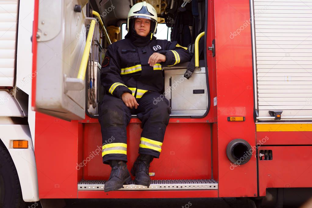 Photo of fireman wearing helmet sitting in fire truck at fire station
