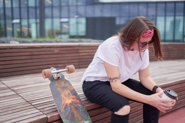 Yaz günü kaykay yakınında ahşap bankta oturan elinde cam ile spor esmer Portresi